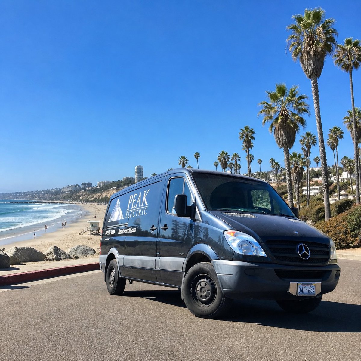 Peak Electric service van parked on a coastal road with a beach and palm trees visible in the background